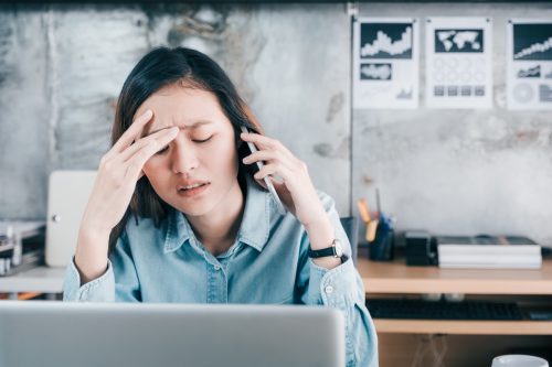 Stressed creative designer woman cover her face with hand and feel upset while talk on mobile phone with customer in front of laptop computer