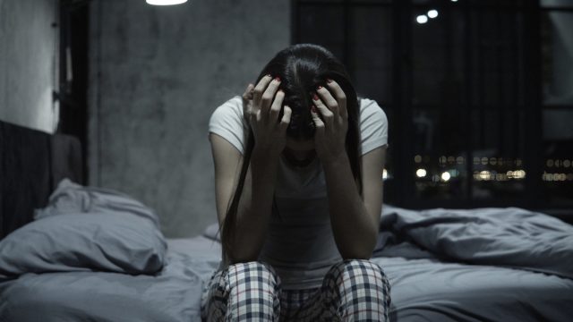 Young woman can't sleep, covering face with hands