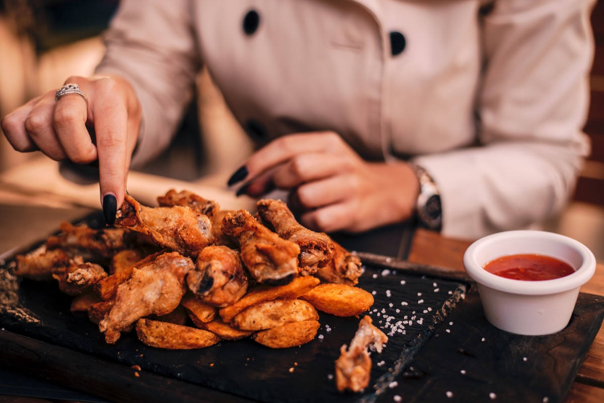 Closeup of girl's hands eating chichen wings. Food photography.
