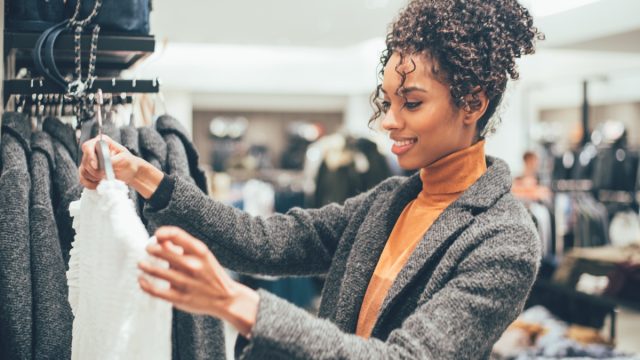 woman with curly hair in orange turtleneck and gray sweater clothing shopping