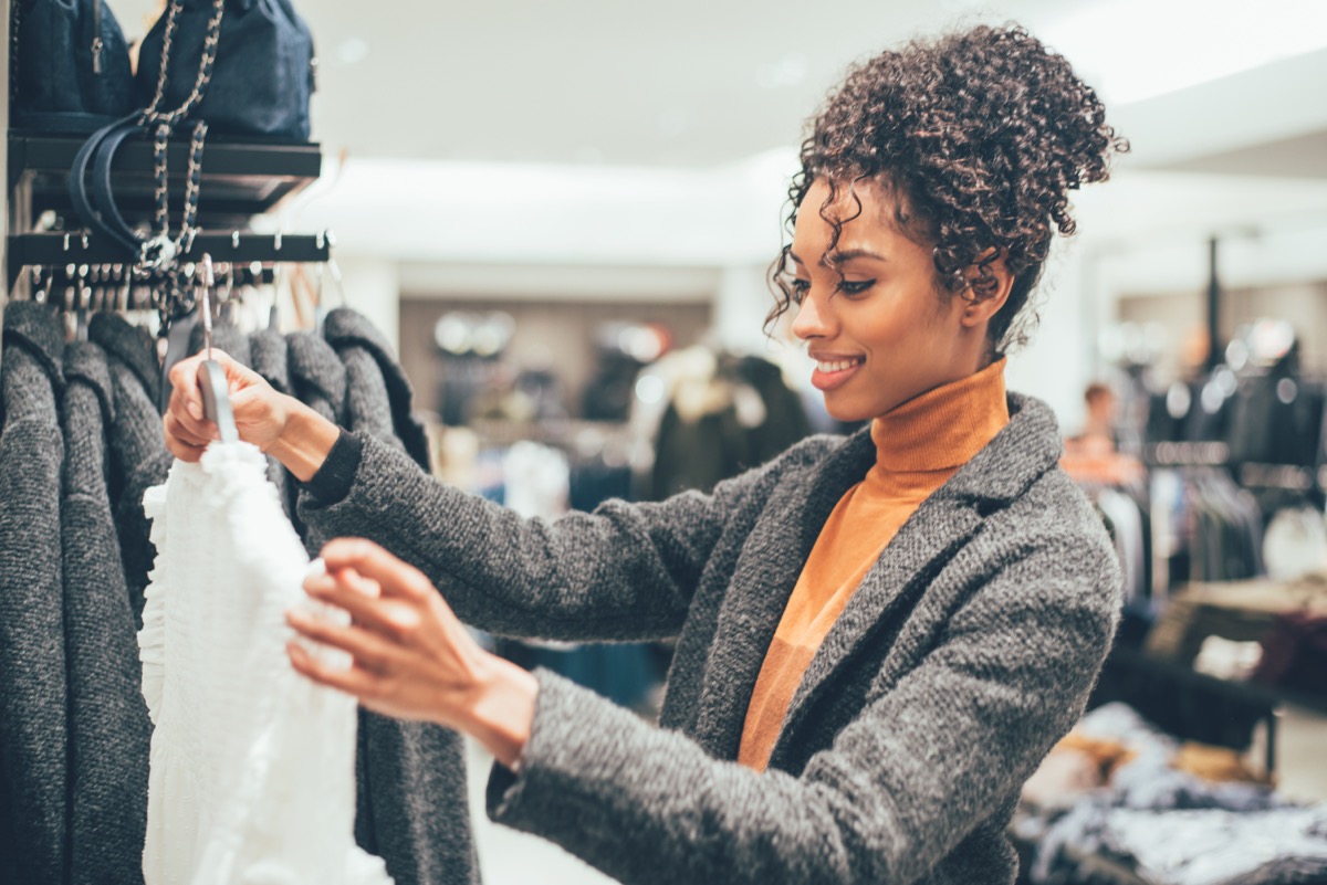 woman with curly hair in orange turtleneck and gray sweater clothes shopping