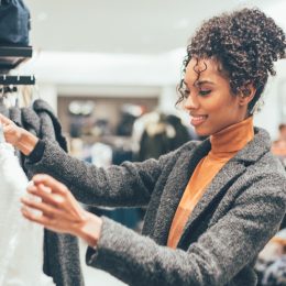 woman with curly hair in orange turtleneck and gray sweater clothing shopping
