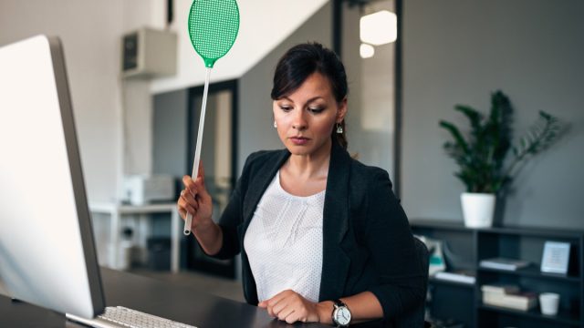 woman holding green flyswatter at desk