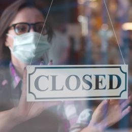 woman in face mask hanging closed sign in restaurant window