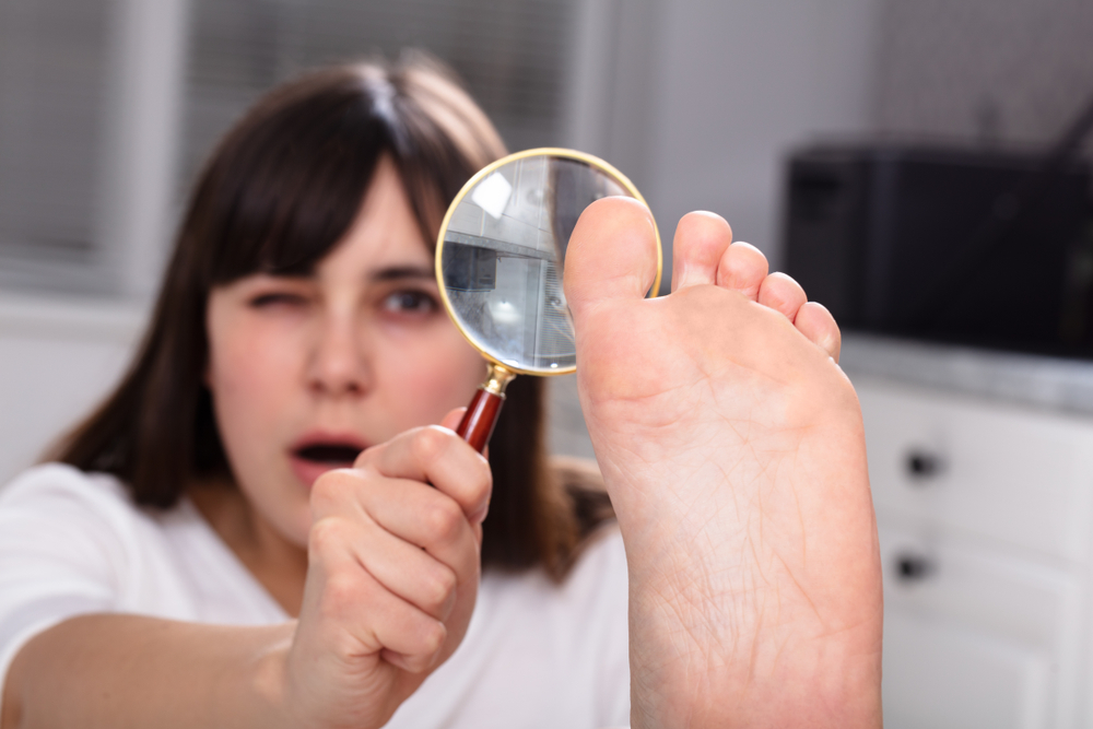 A young woman looking at her toes with a magnifying glass