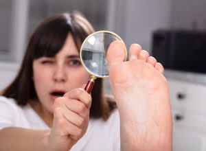 A young woman looking at her toes with a magnifying glass