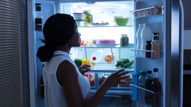 young woman opening the fridge at night in dark kitchen