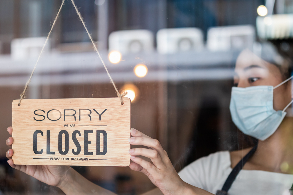 A woman wearing a mask putting up a closed sign on the door of a restauratnt