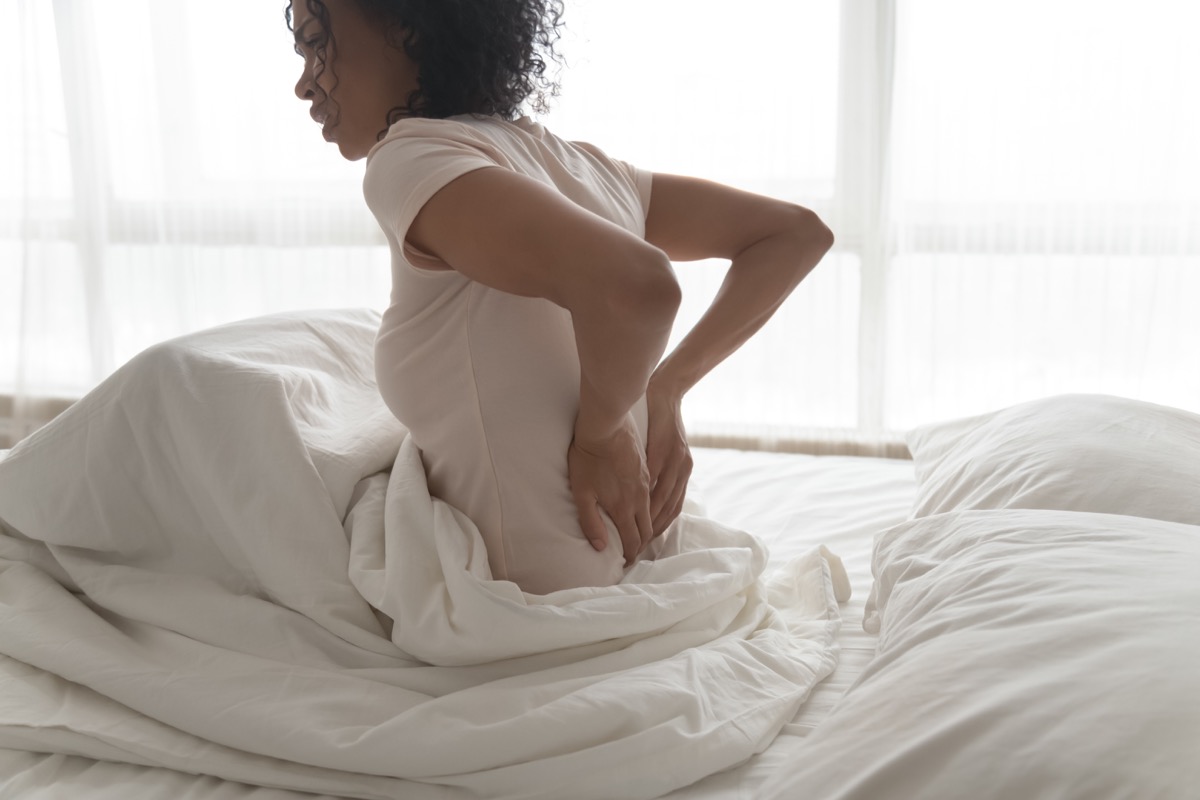 người phụ nữ bị đau lưng sau khi thức dậy, chạm vào các cơ xoa bóp cọ sát, cô gái cảm thấy khó chịu do tư thế xấu hoặc giường không thoải mái