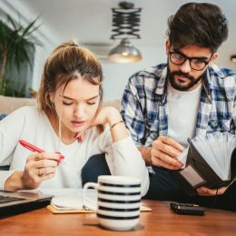 A young man and woman sit on the couch while going over forms to file taxes