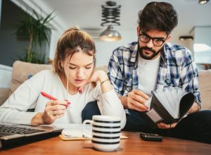 A young man and woman sit on the couch while going over forms to file taxes