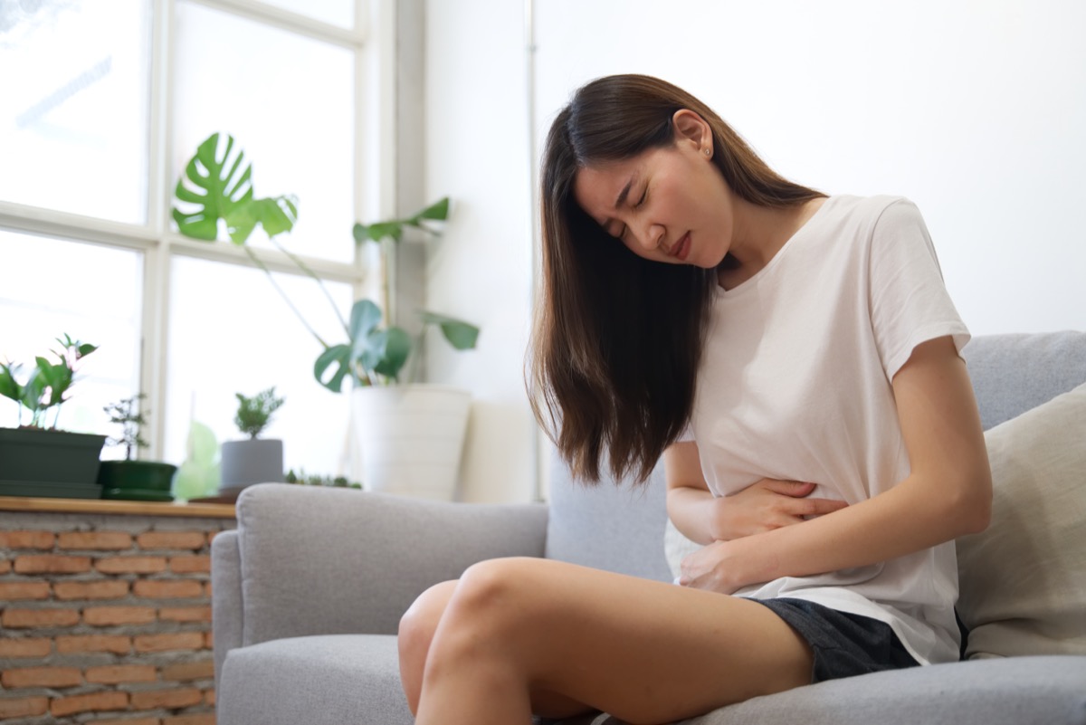 young woman sitting on couch with stomach pain