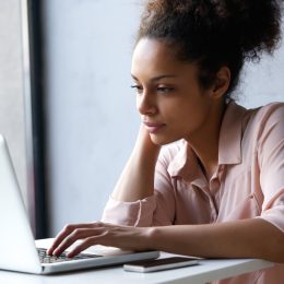woman in her 20s or early 30s using laptop while wearing pink button down shirt