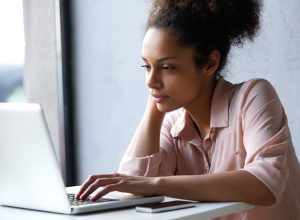 woman in her 20s or early 30s using laptop while wearing pink button down shirt