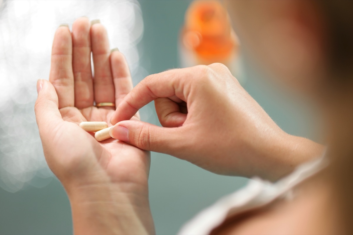 Vue rapprochée d'une jeune femme tenant des pilules de vitamines et de minéraux de ginseng à la main avec une bouteille de capsule sur la table.  vue grand angle