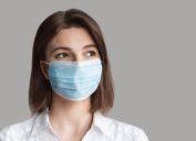 Masked woman patient isolated on a gray background, copy space. Epidemic, pandemic, corona virus protection, healthy lifestyle, self-care, people concept