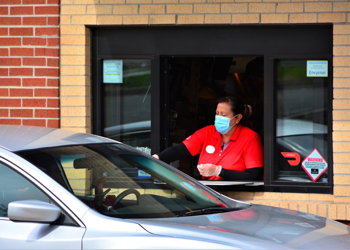 Denver, CO, USA. May 12, 2020. Fast food worker at Chick-Fil-A restaurant in Denver serving food to a drive thru customer while wearing her face mask.