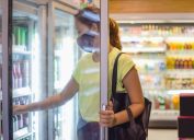 woman with face mask opening freezer door, taking some cold drinks in convenience store during Covid 19 pandemic