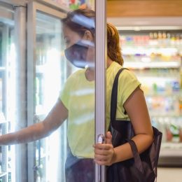 woman with face mask opening freezer door, taking some cold drinks in convenience store during Covid 19 pandemic