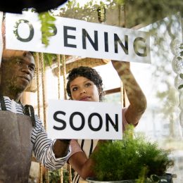 Two workers placing an opening soon sign on the window of a store