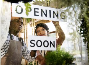 Two workers placing an opening soon sign on the window of a store