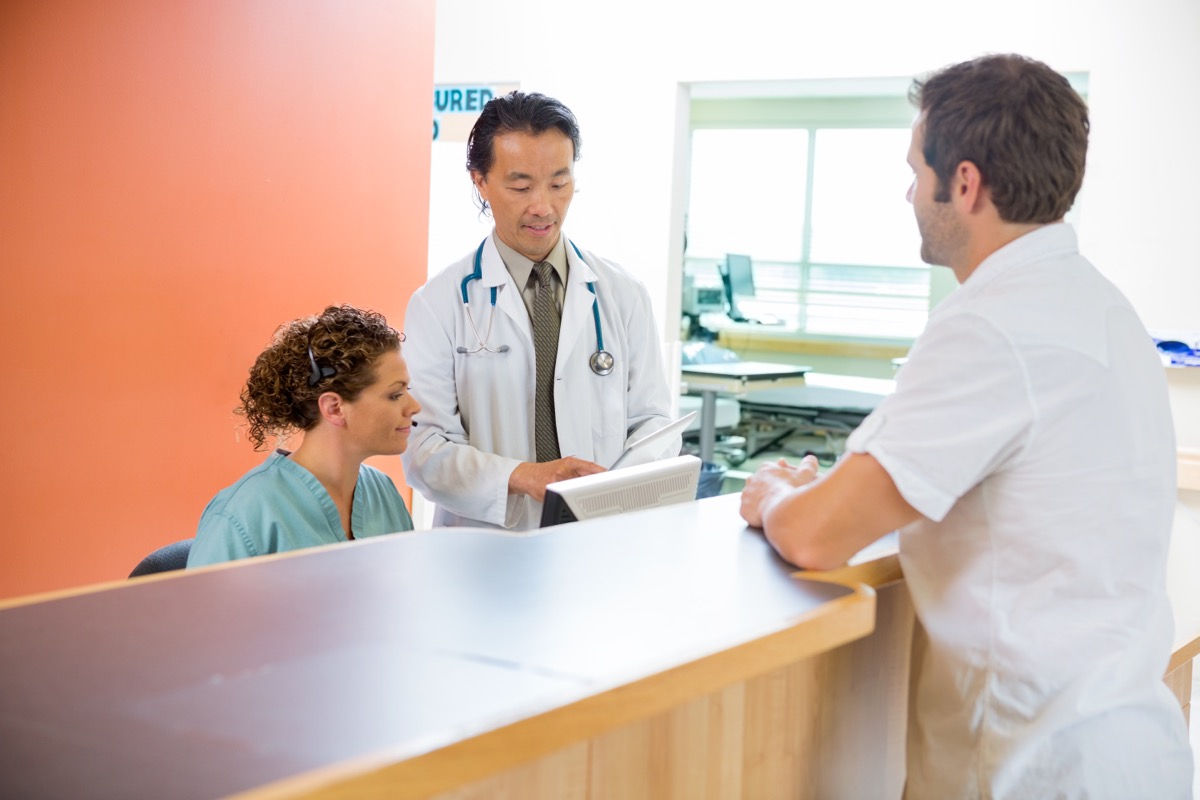 unmasked doctor and nurse talking to male patient at reception desk