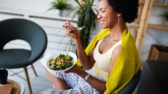 woman, sitting with bowl of salad, eating, smiling