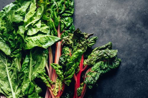 A pile of leafy greens including spinach and chard on a black background