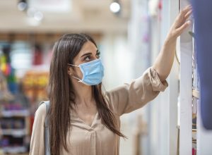 Young woman shopping in a grocery store and wearing protective medical mask. Women with face mask for protection against influenza virus shopping. Shopping in supermarket