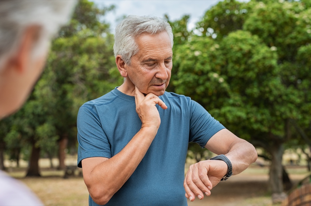 Възрастен уморен мъж проверява пулса след тренировка.  Старец измерва пулса на пулса на врата си и гледа спортен часовник.  Възрастният мъж умножава пулсациите в парка.