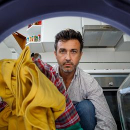 Middle-aged man putting clothes in the washing machine. View from inside.