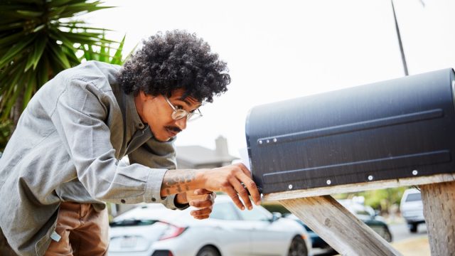 man looking into mailbox in street