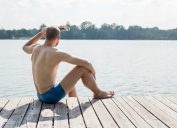 man in swim trunks looking out at lake