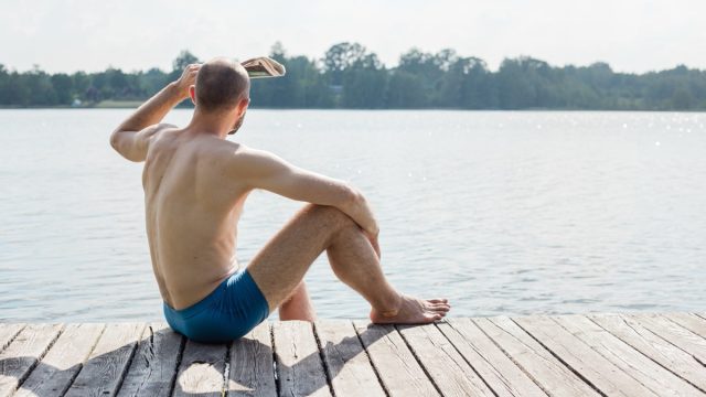man in swim trunks looking out at lake