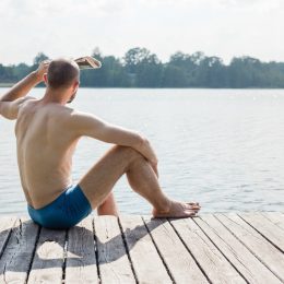 man in swim trunks looking out at lake