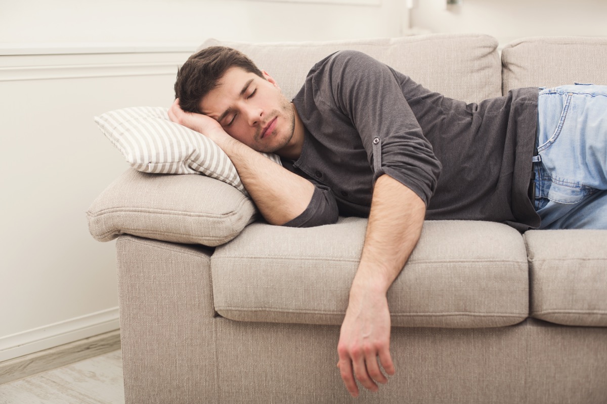 Young casual man sleeping on couch at home during day time