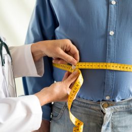 doctor measuring overweight man's waist