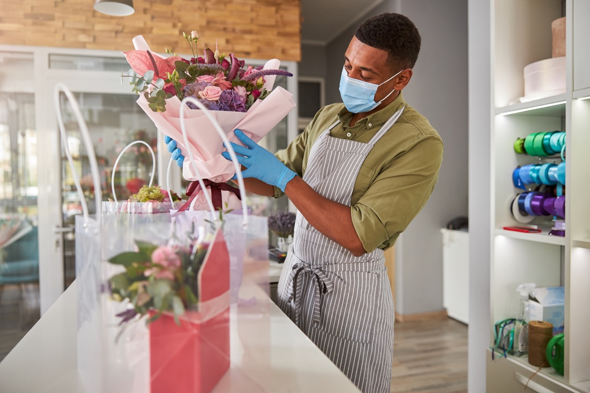 Focused shop manager with a face mask placing a bunch of flowers in a light purple container
