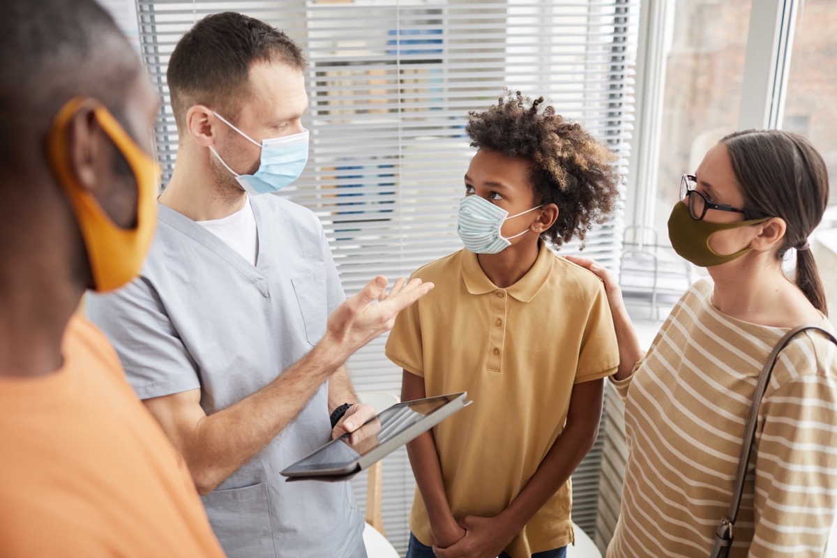 parents and young male child talking to doctor while all wearing masks amid covid pandemic