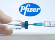 A set of hands filling a syringe from a vial in front of the Pfizer logo