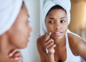 shot of a young woman inspecting her skin in front of the bathroom mirror and looking upset