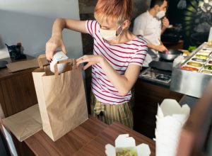 A restaurant worker packing a to-go order into a paper bag