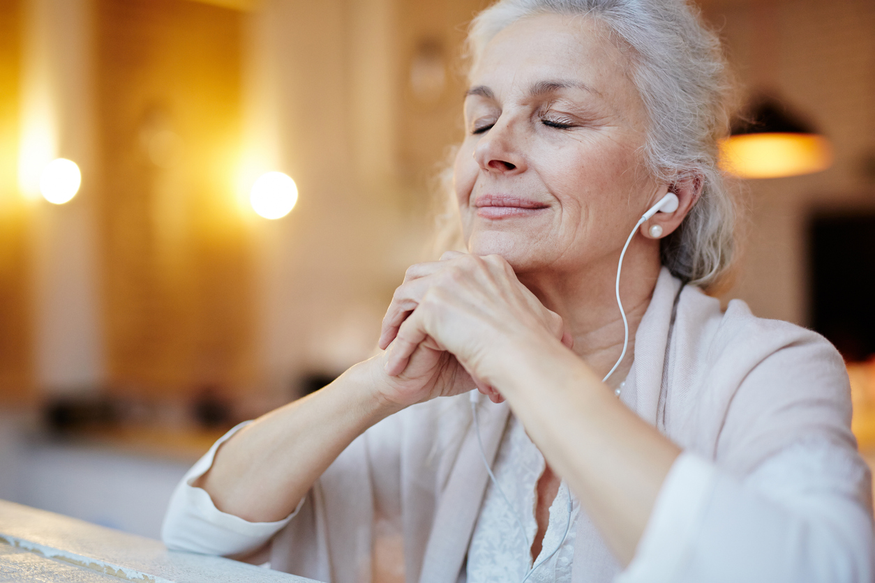 A senior woman sitting with her eyes closed while listening to headphones
