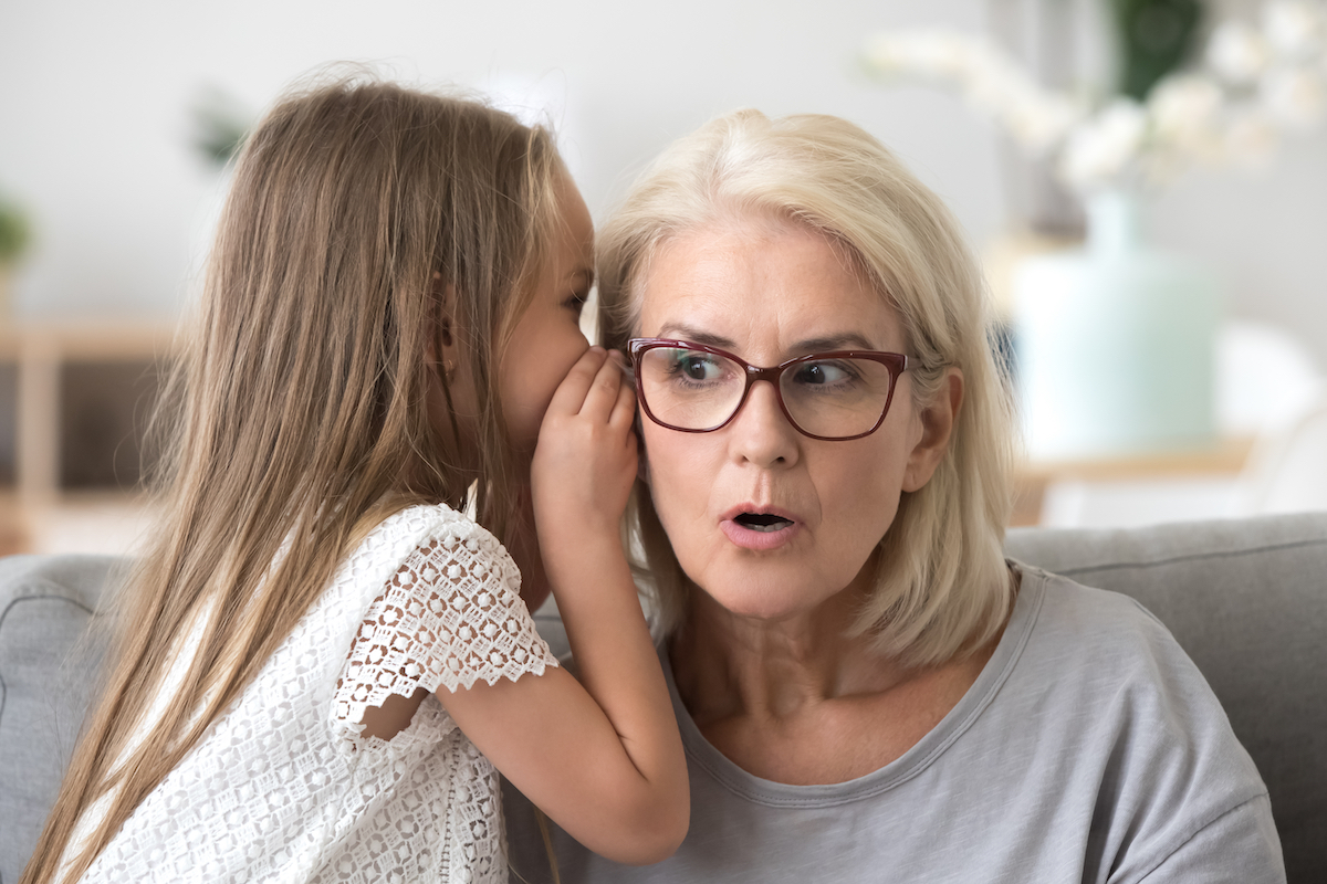 Girl whispering in surprised grandmother's ear