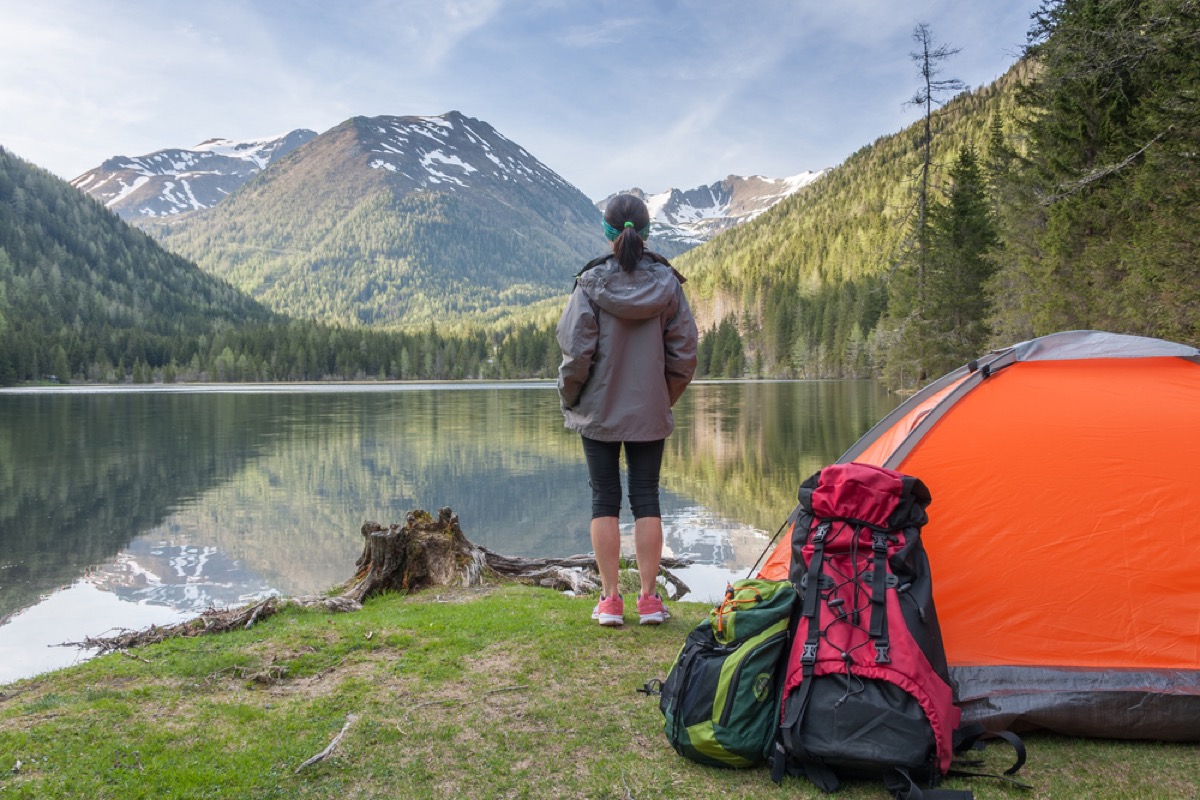 woman at lake with tent and backpack in foreground