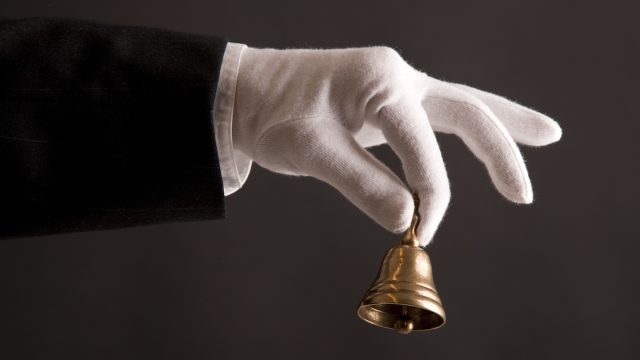 butler's hand in white glove holding a small bell