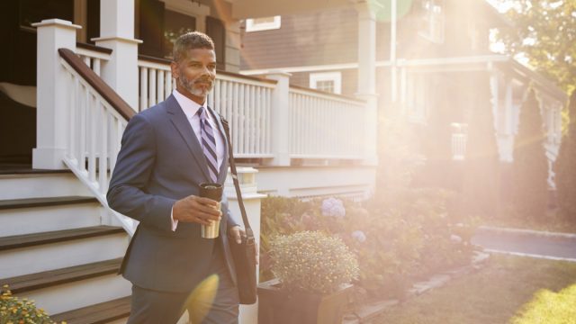 Businessman With Cup Of Coffee Leaving Suburban House For Work