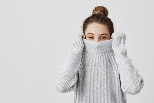 Portrait of young woman pulling her sweater over head and smelling it