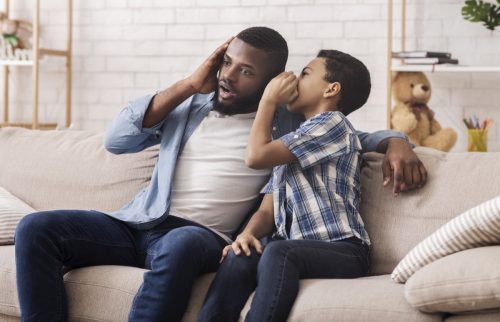 a boy shares a secret with his dad while sitting on couch