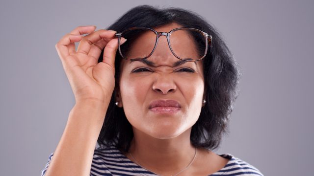 Woman struggling to see without her glasses against a grey background